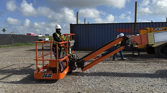 JLG boom lift extended across a construction site with a worker elevated in the platform.